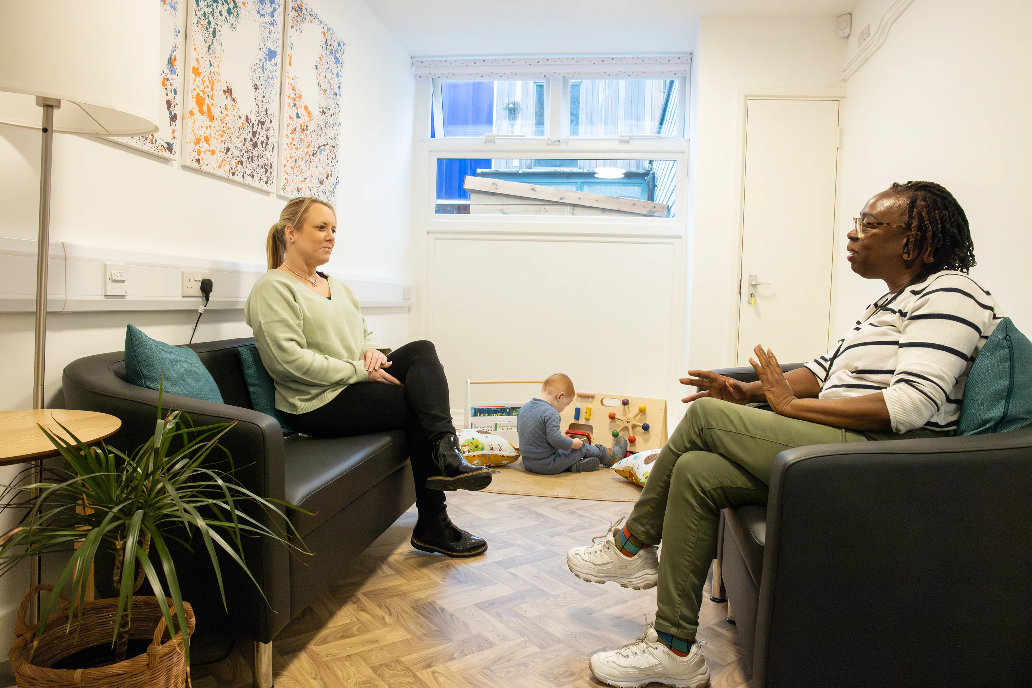 Mother talking to family worker while child plays.